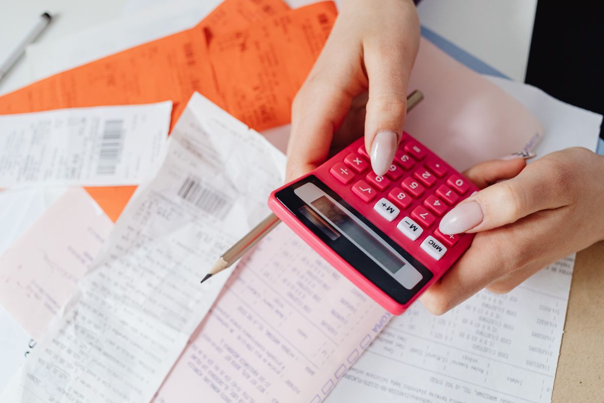 Hands adding up household receipts on a pink calculator, the way to total ten years of water softener running costs