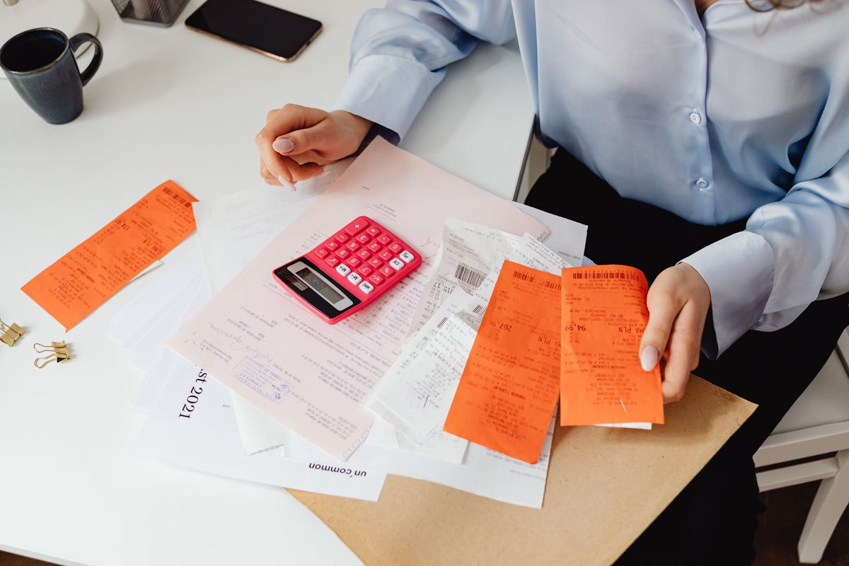 Woman at a desk reviewing a pile of receipts with a calculator, the kind of cost check that reveals a softener using far more salt than it should