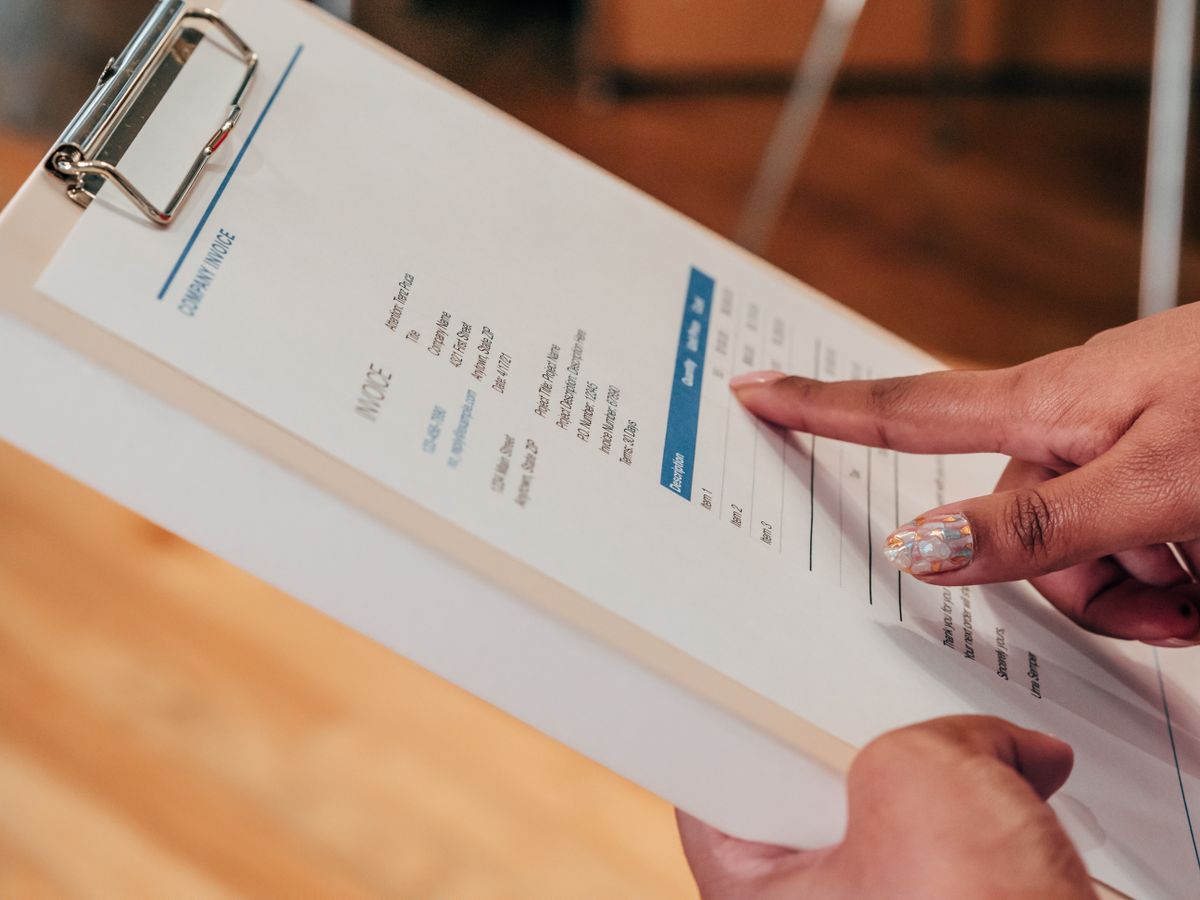 Person pointing at the line items on an itemized invoice held on a clipboard, the way to read a water softener quote before signing