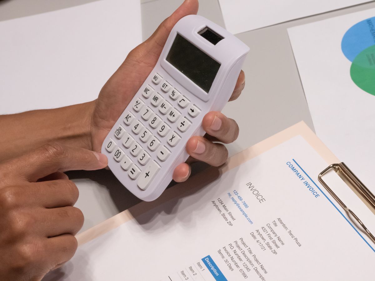 Hands holding a calculator over a printed service invoice, adding up a year of water softener maintenance costs
