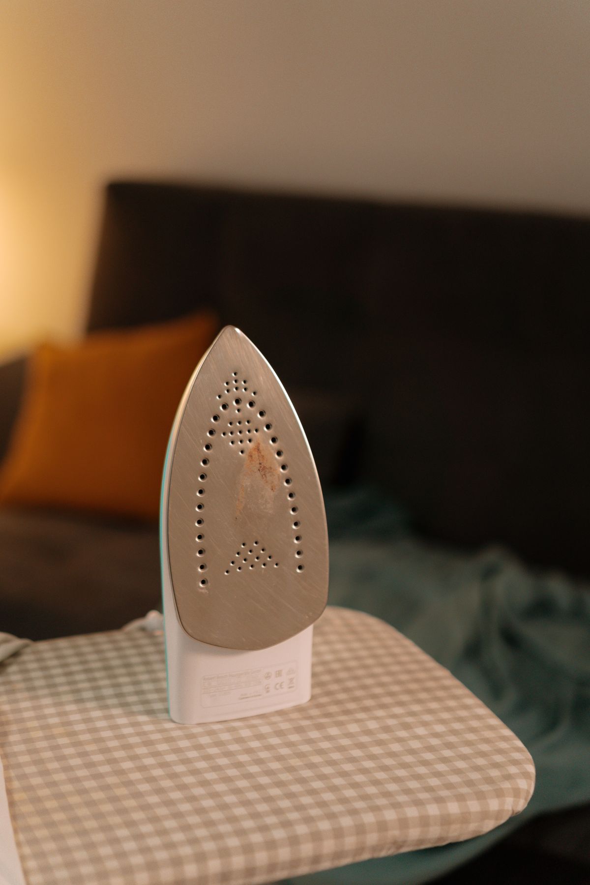 Clothes iron standing on its heel on a gingham ironing board, showing the steam vents in its soleplate