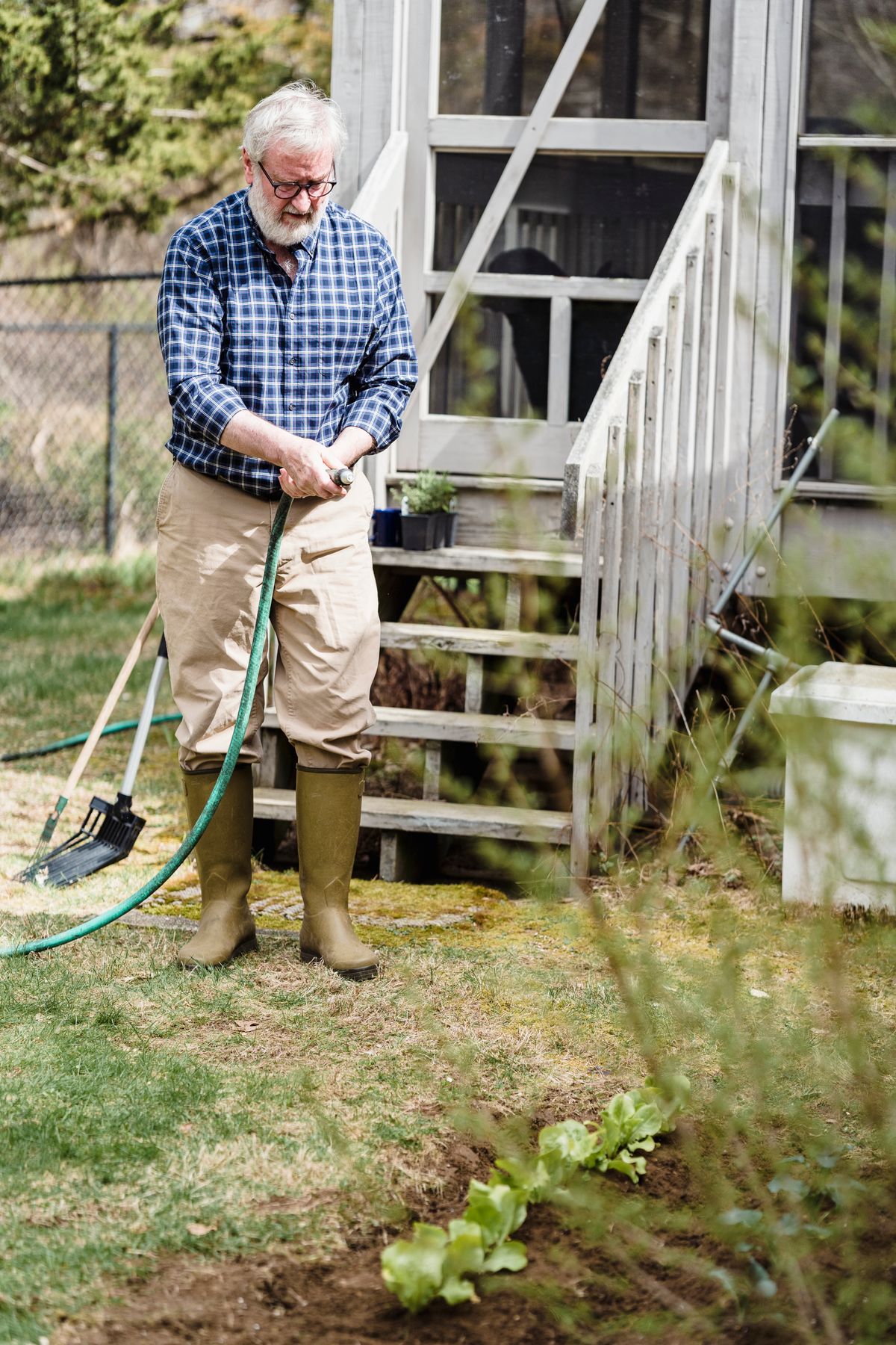 Gardener watering a vegetable bed with a garden hose in a backyard