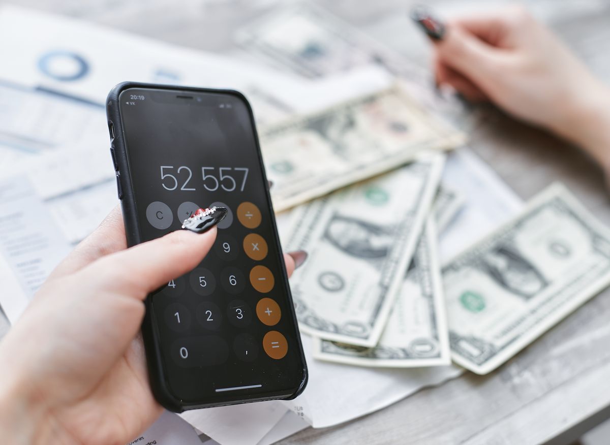 Hand holding a smartphone calculator over US dollar bills and printed statements, converting a monthly water softener payment into its cash price