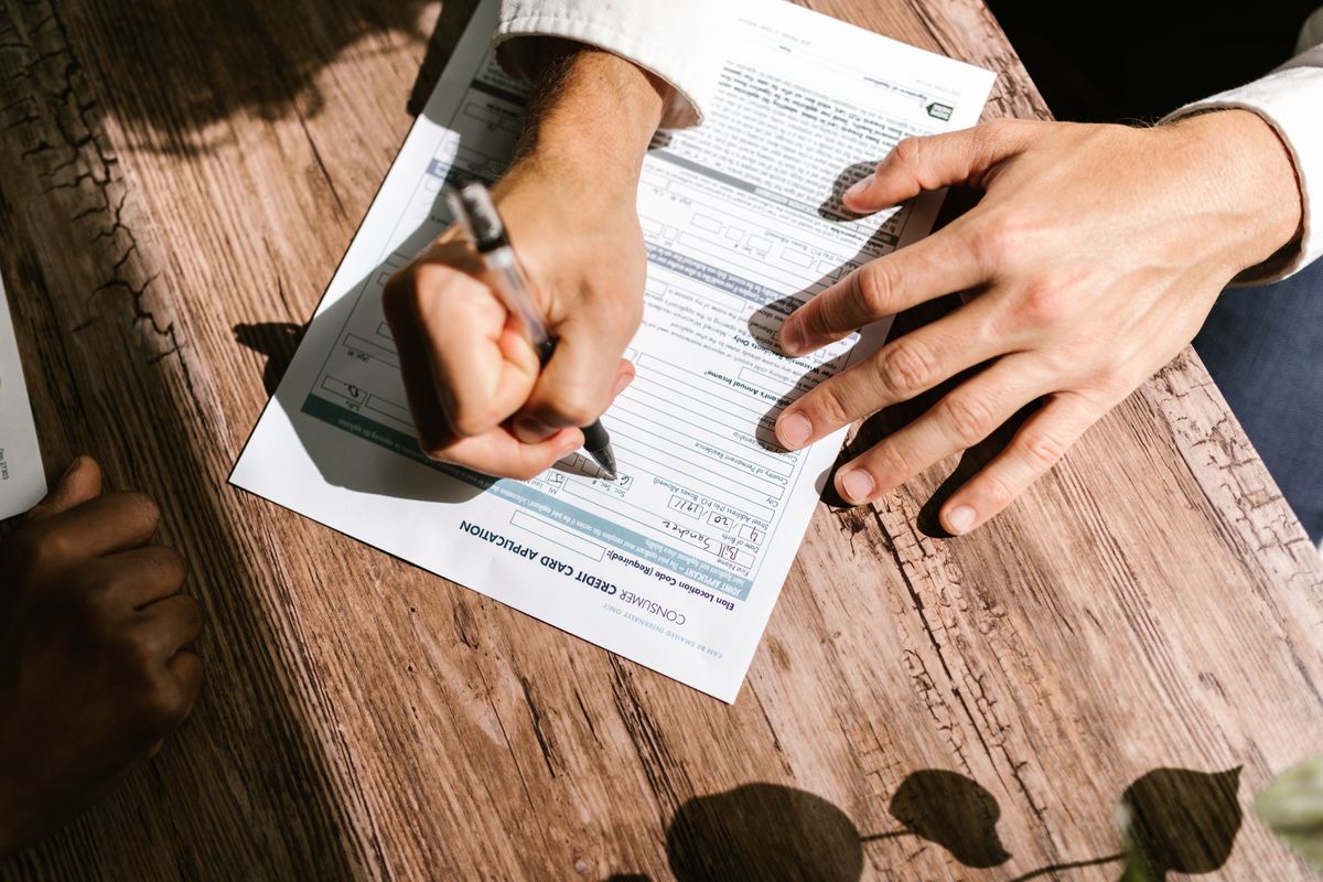 Two people filling in a consumer credit card application at a wooden table, the store-card application many water softener financing promotions start with
