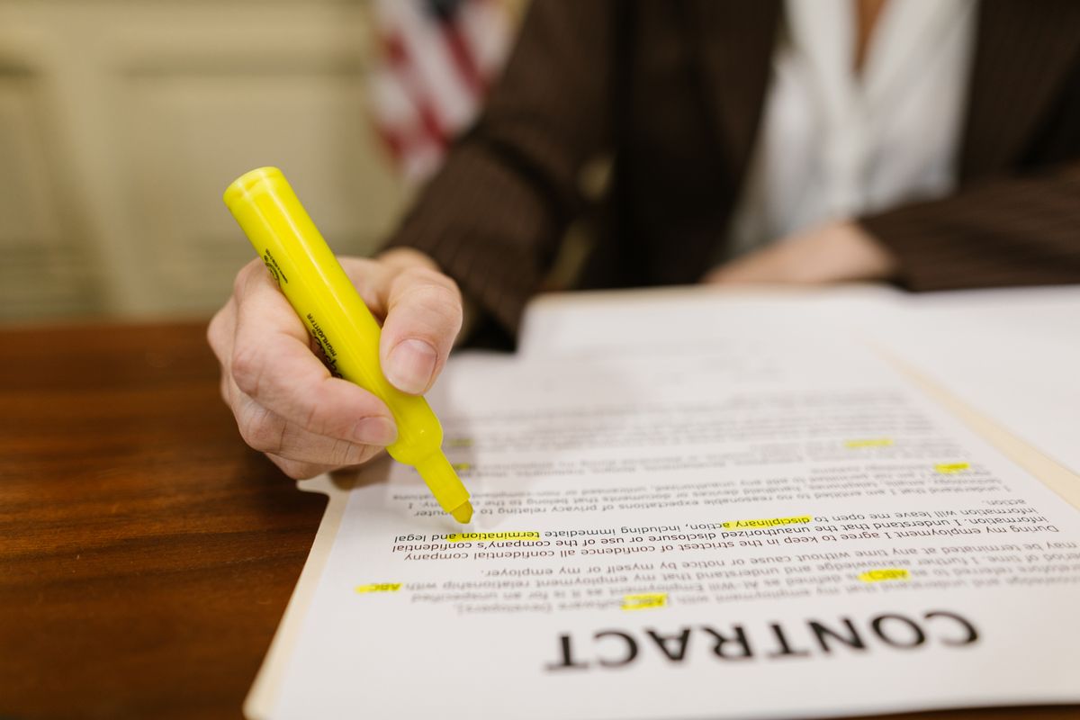 Hand marking key clauses of a printed contract with a yellow highlighter before signing