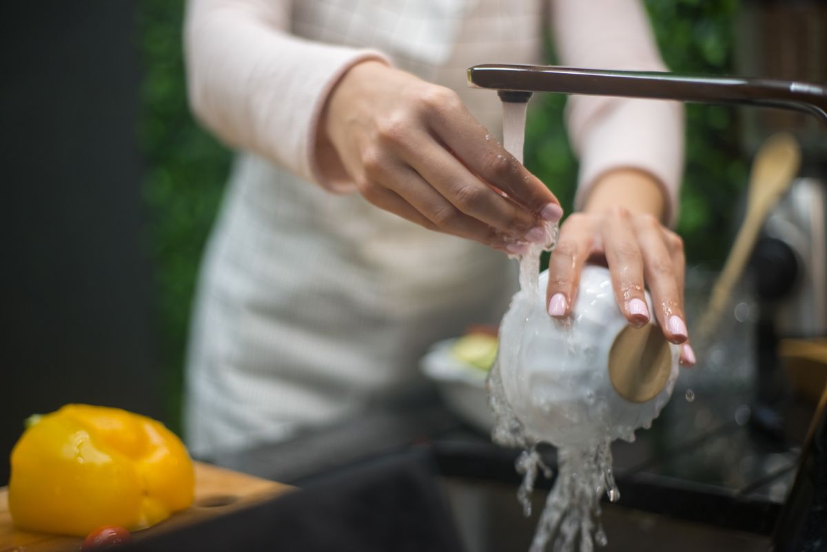 Hands rinsing a white bowl under a running kitchen faucet, everyday household water use that counts toward a softener's capacity