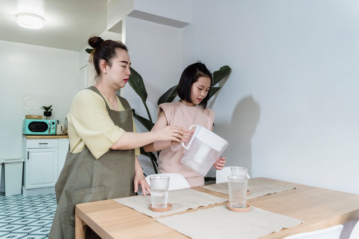 Parent and child filling a glass from a filter jug at the kitchen table, the usual household response to a chlorine taste