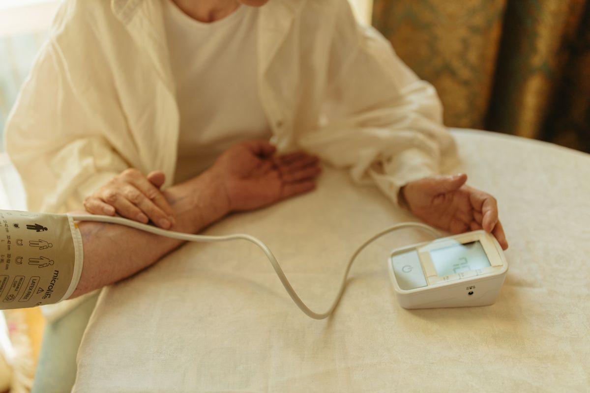 Senior adult checking blood pressure with a digital monitor at home, a reading the clinician weighs when setting a sodium limit