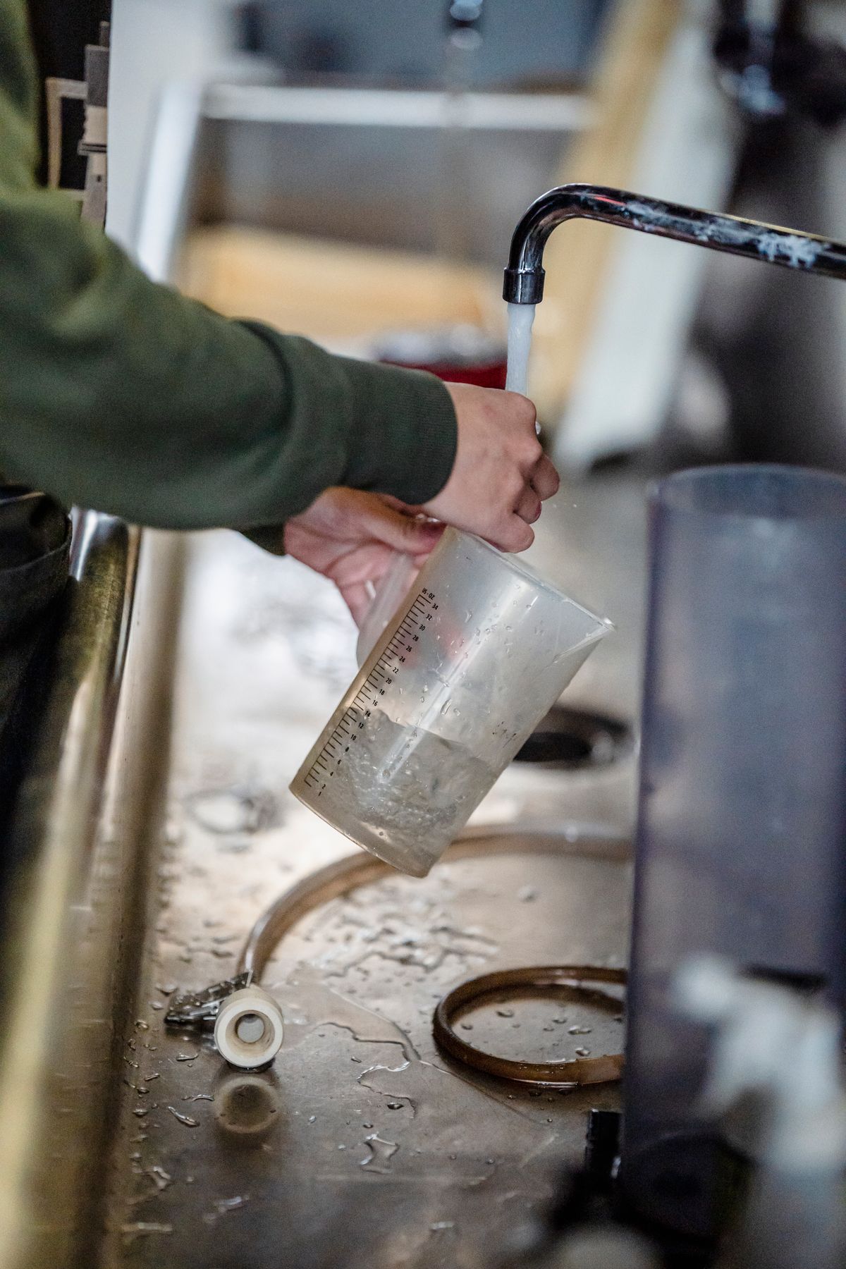 Hand filling a graduated measuring jug from a scaled tap, the moment most water hardness sampling mistakes happen