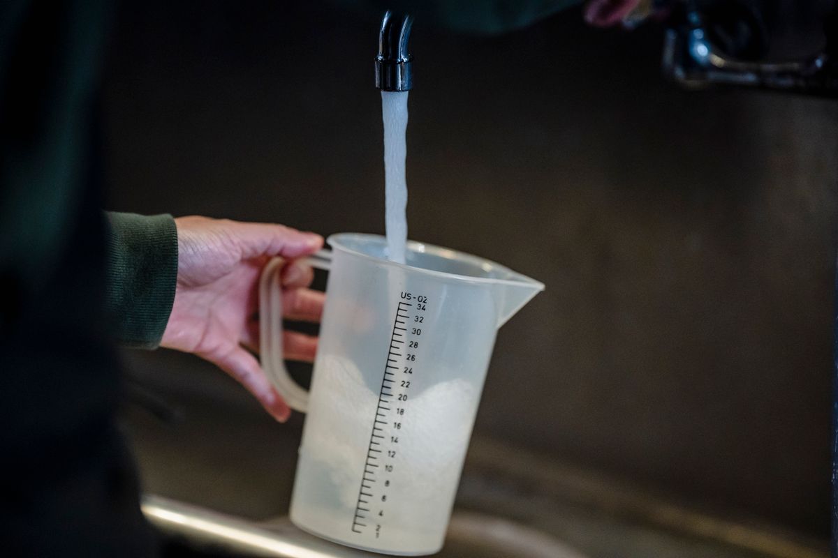 Hand holding a measuring pitcher under a running faucet, the known-volume draw used to test whether a softener's water meter is counting