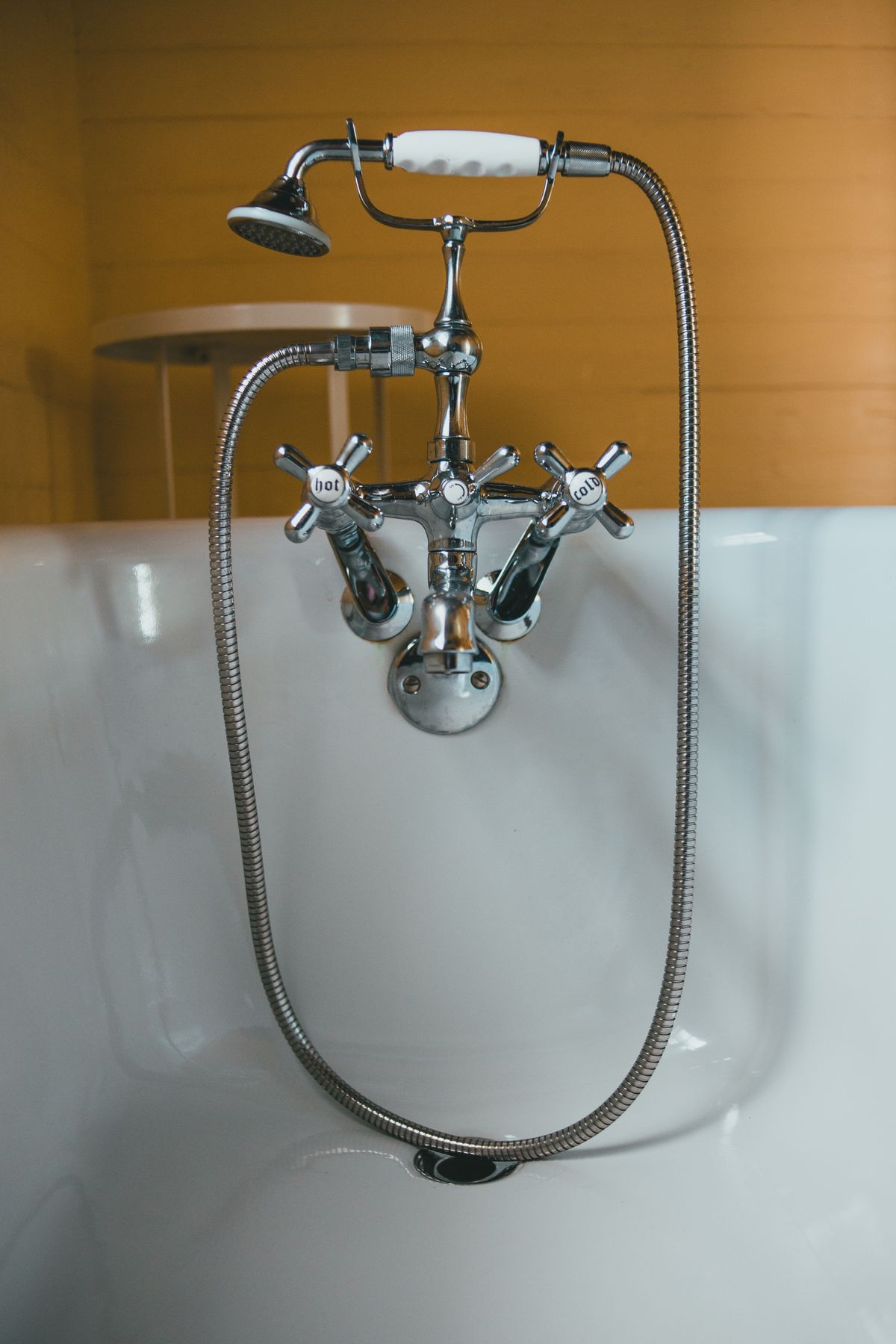 Chrome bath mixer with white hot and cold cross handles and a hand shower on a white tub, the kind of hot-water outlet where hard water scale builds first
