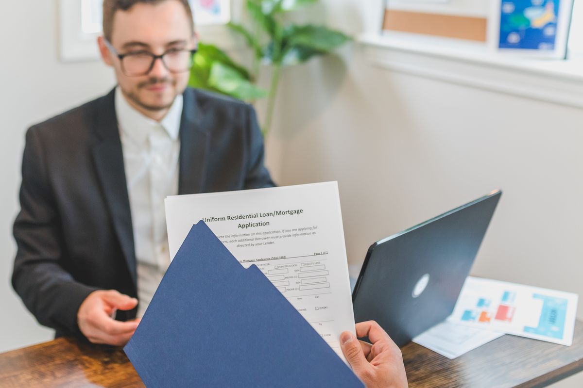 Salesman in a suit holding a printed finance application across a desk, as when a RainSoft water softener quote is presented as monthly payments