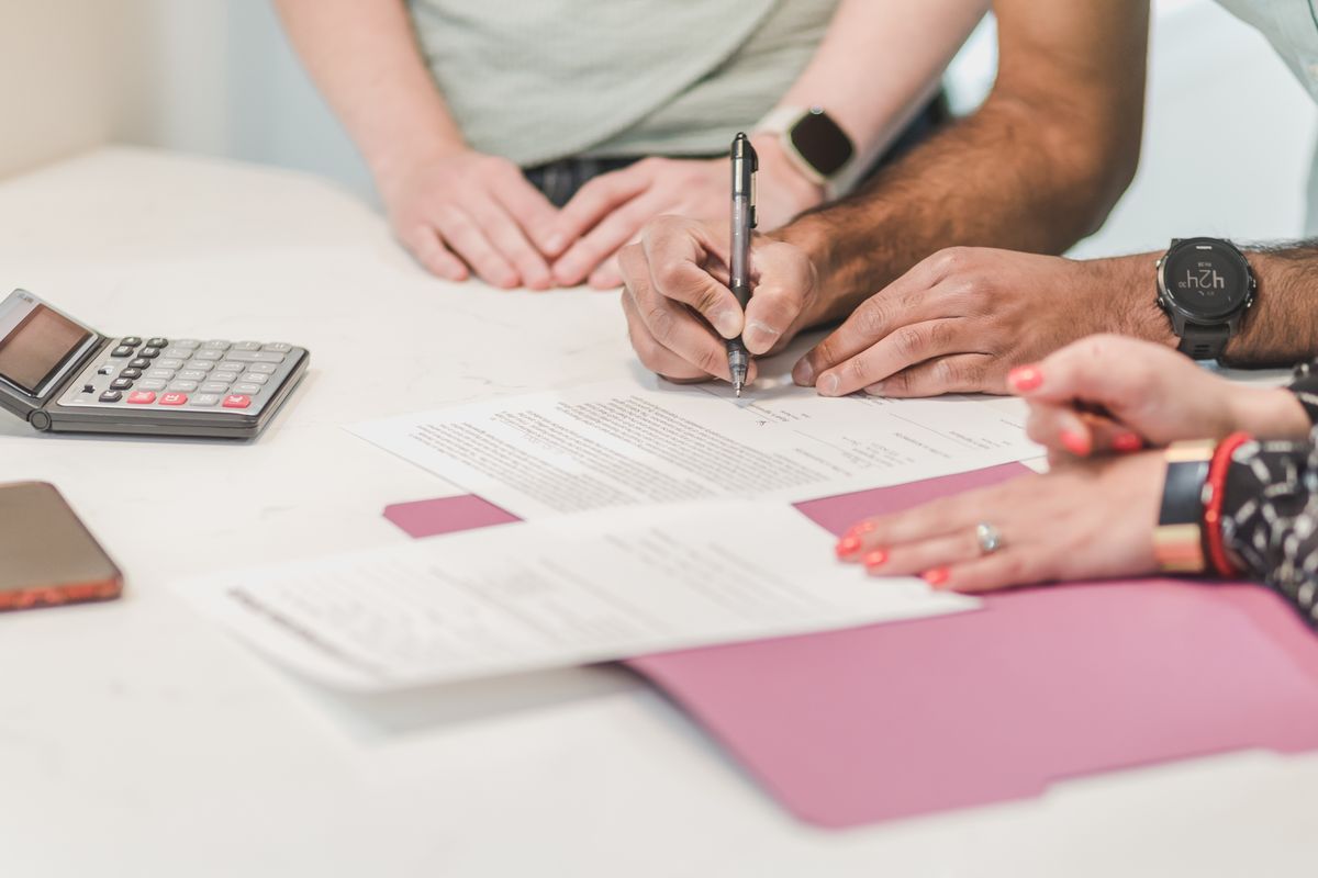 Two people signing a printed agreement on a desk with a calculator beside it, the moment to confirm the regular rate, salt delivery and removal fee on a softener rental