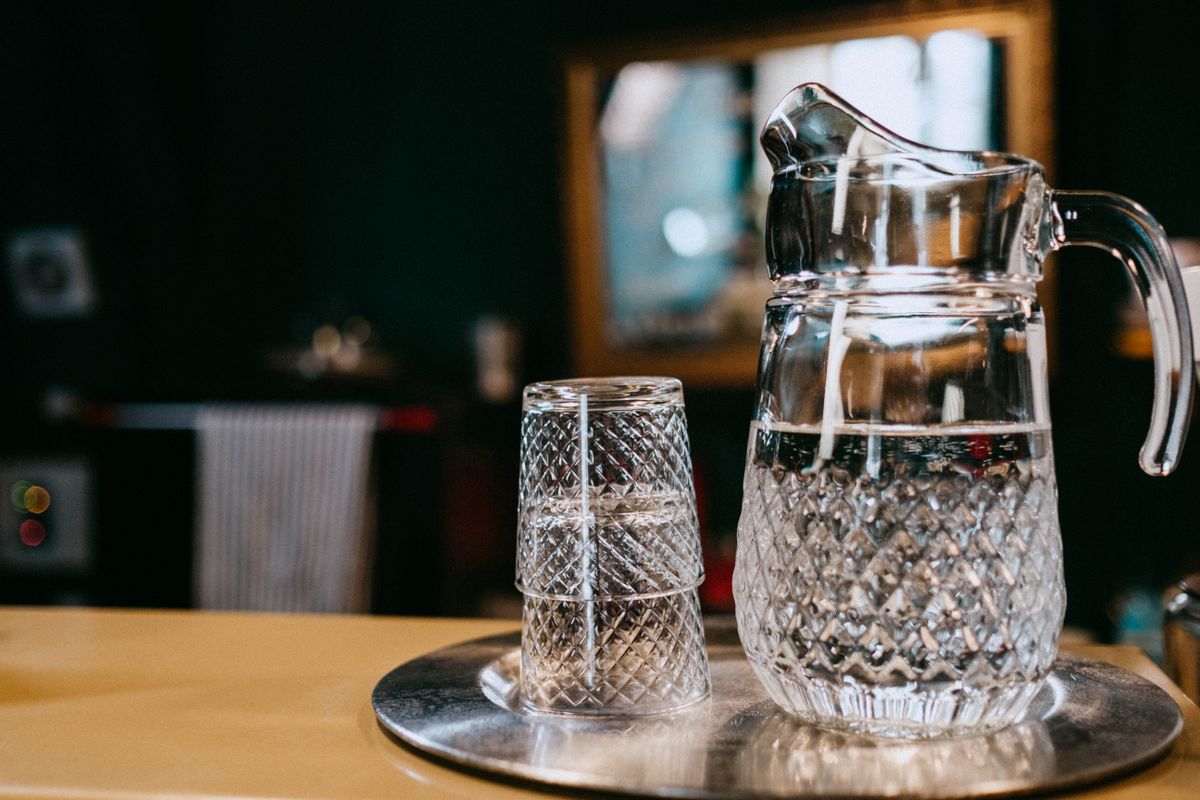Crystal glass water pitcher and two cut-glass tumblers on a steel tray, the low-sodium drinking water an RO faucet delivers from softened feed