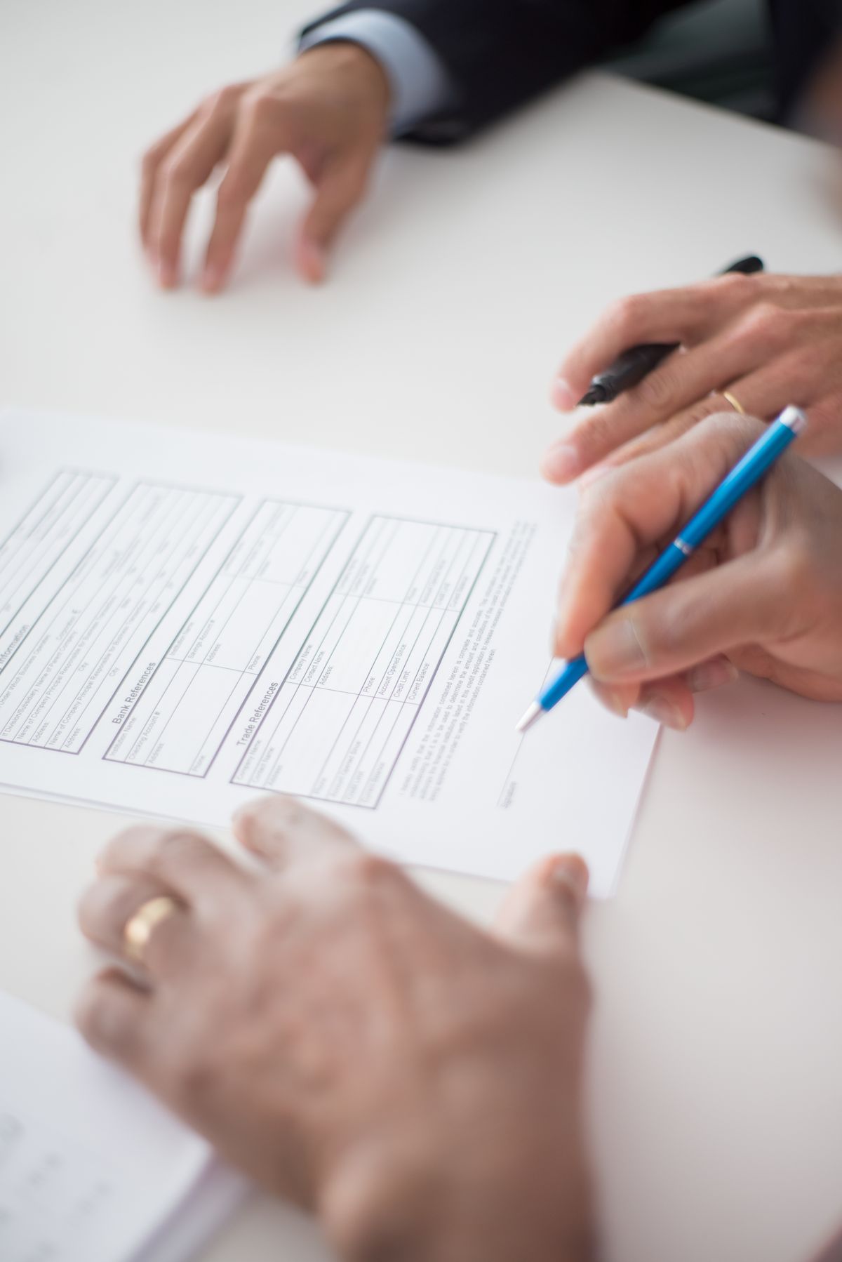 Two people at a table, one filling in and signing a printed agreement form with a blue pen