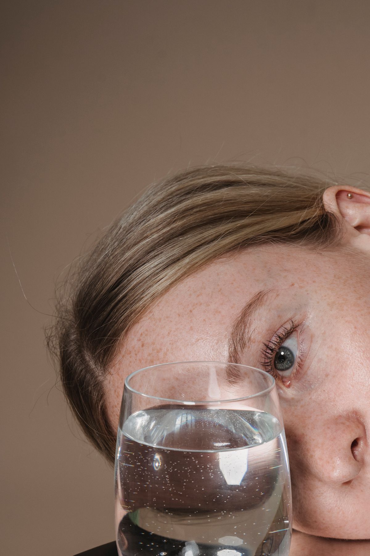 Woman resting her head on a table and studying a glass of water at eye level, the close look that tells dissolved iron from oxidized iron