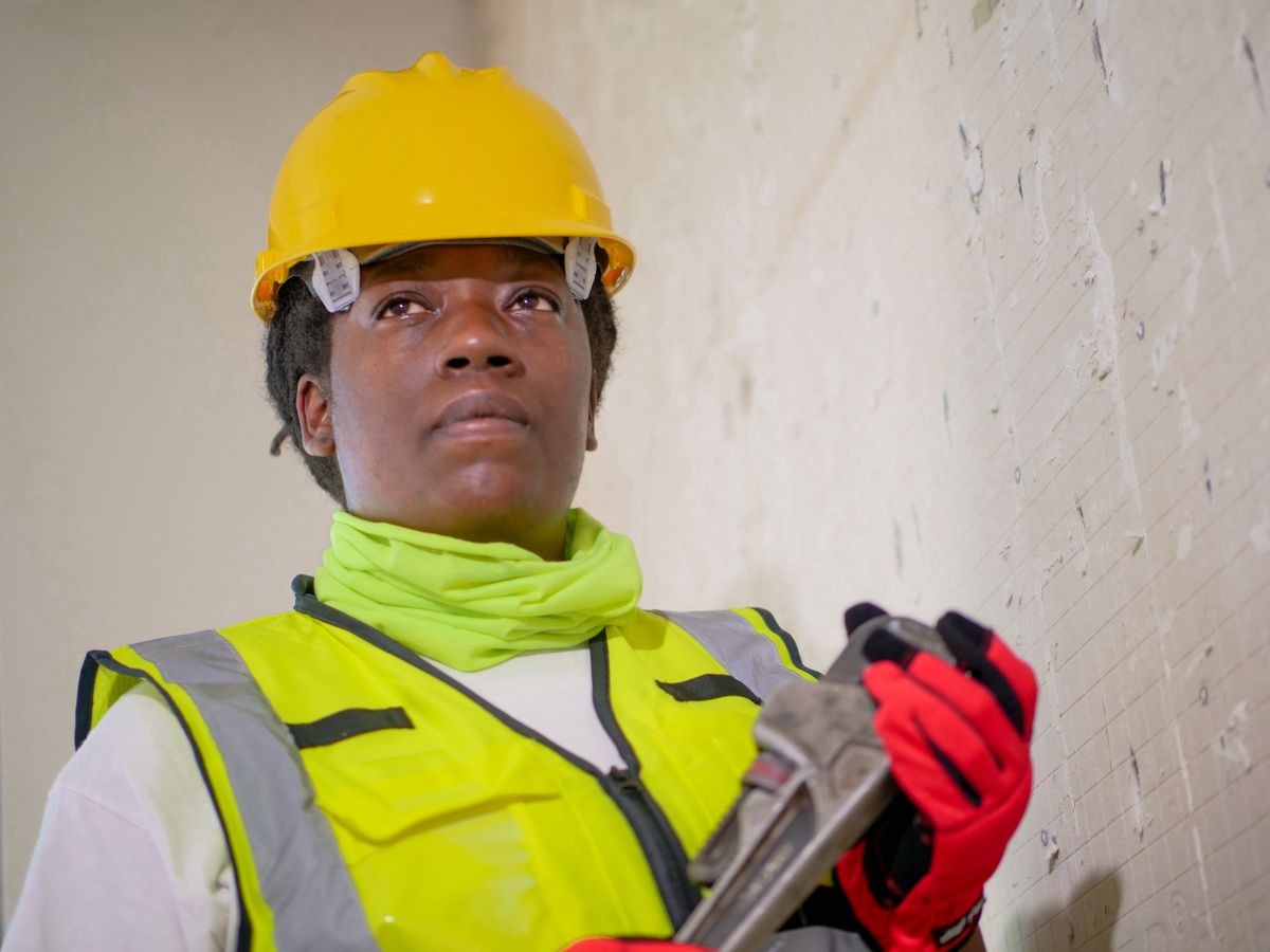 Worker in protective equipment holding a wrench indoors, the service visit where a re-bed or replacement decision gets made
