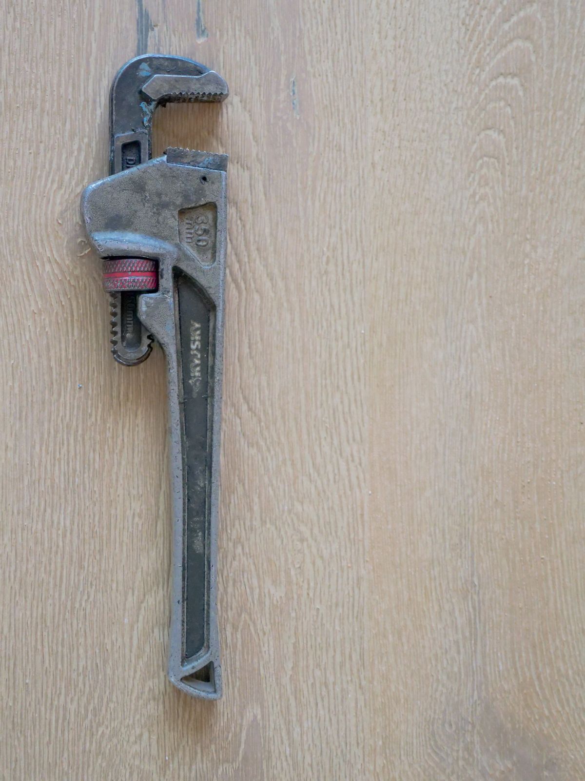 Metal plumber's wrench resting on a wooden surface, the tool used to loosen fittings when removing and cleaning a softener injector