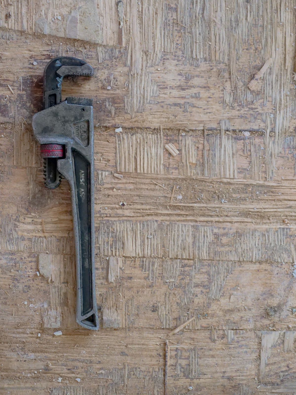 Vintage pipe wrench lying on a rustic wooden surface, the basic hand tool needed to open fittings and clear debris from a softener inlet
