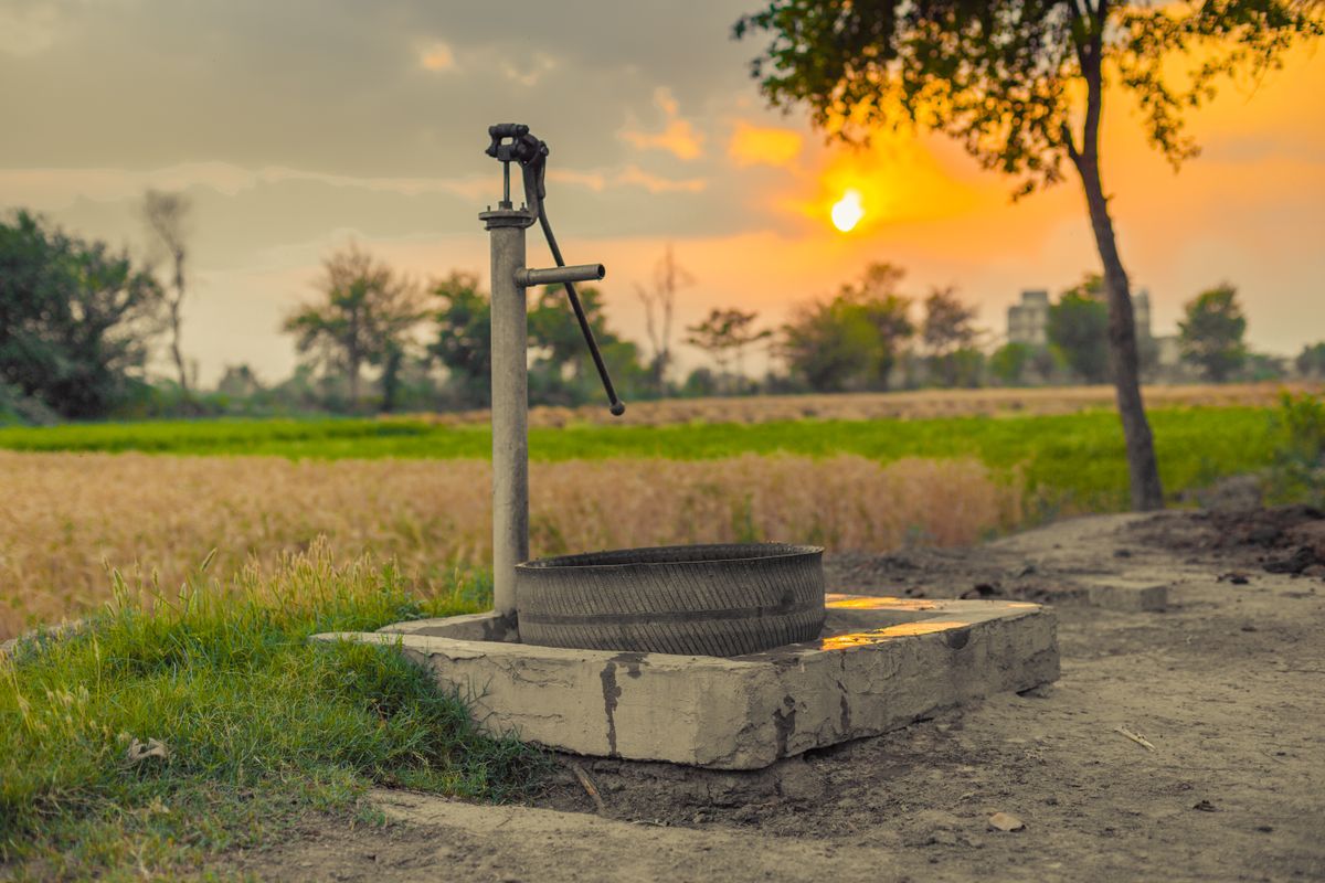 Cast iron well pump standing in an open field at sunset, the water source a private well hardness test has to characterise