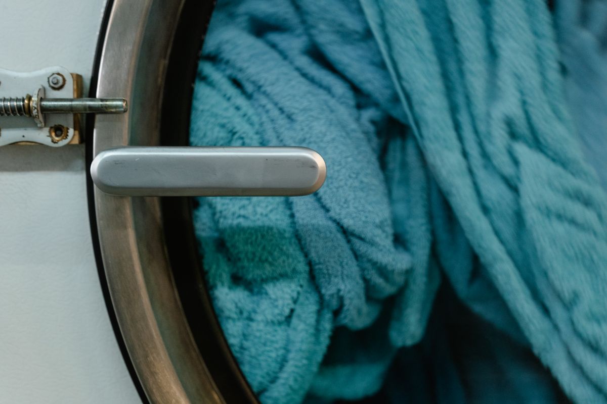 Front-loading washing machine door with blue towels inside, the appliance a renter can feed with soft water from a hose-connected portable softener