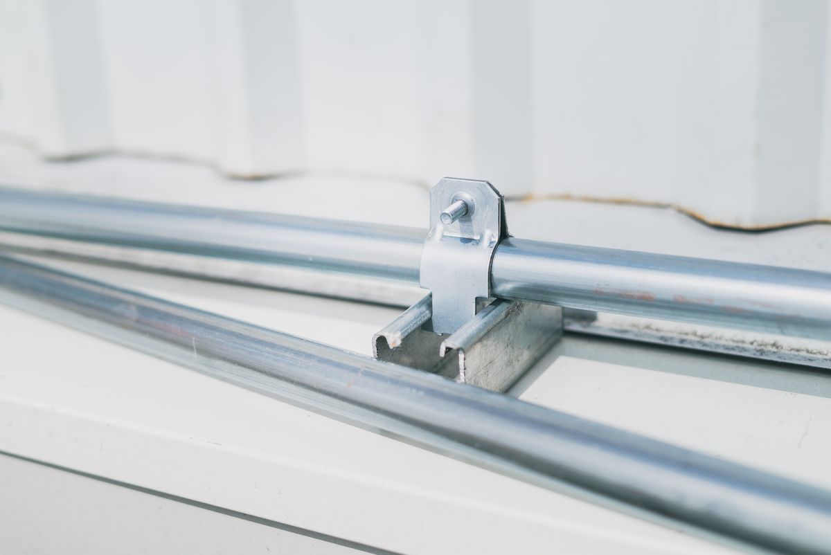 Close-up of a metal pipe clamp on a stainless steel surface, the type of band clamp that holds softener drain tubing on its barb and slowly loses grip as the plastic creeps