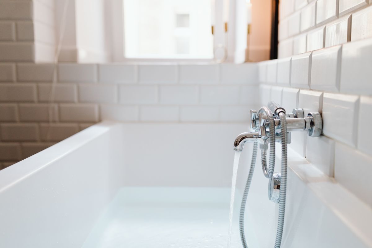 Freestanding ceramic bathtub with a modern faucet, where a genuine slimy film is easier to see than in a shower