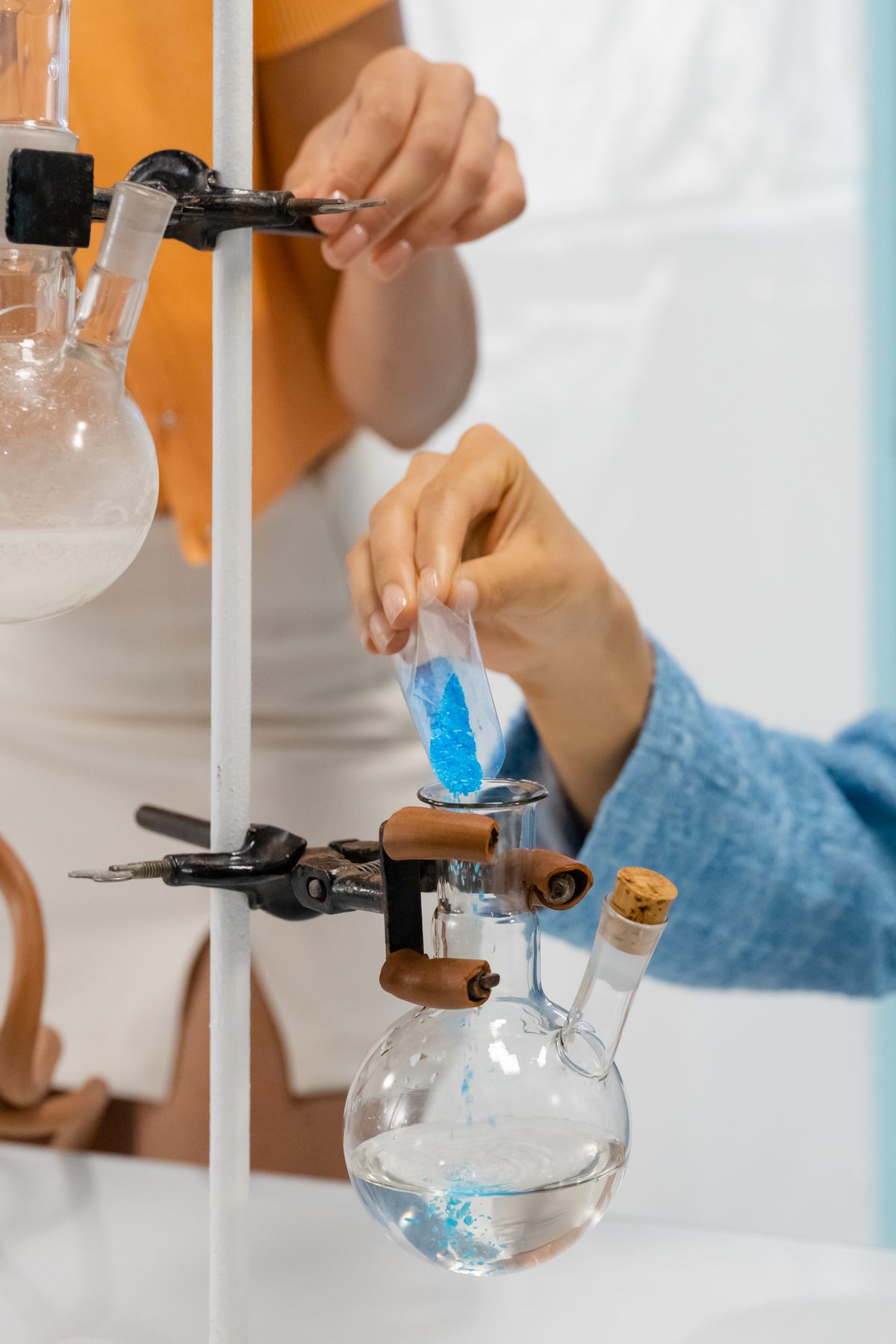 Hand carefully pouring white powder into a glass laboratory apparatus, the kind of measured, recorded approach that a before-and-after resin cleaner test needs