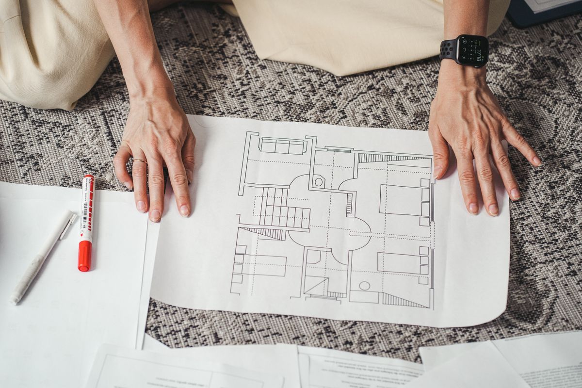 Hands holding and examining a detailed floor plan document, the first step in mapping hardness fixture by fixture