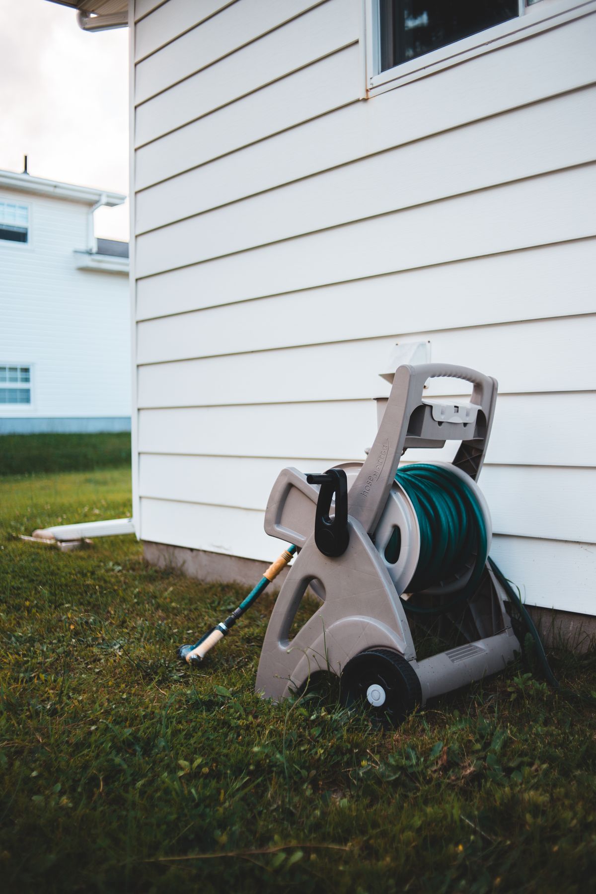 Garden hose on a wheeled reel beside a white-sided house, the outdoor faucet used to flush chlorinated water after a well shock