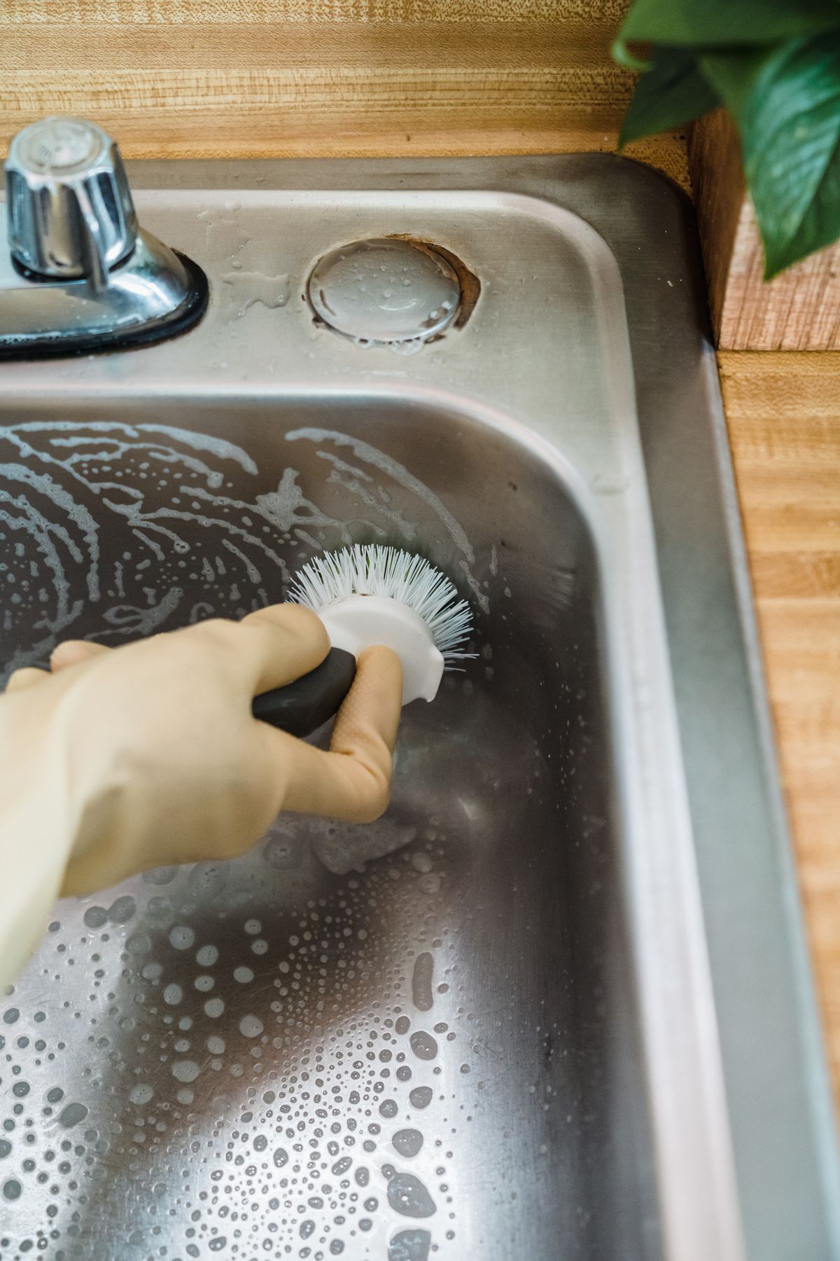 Gloved hand scrubbing a stainless steel basin with soapy water and a brush, the wash stage that follows scraping residue from a brine tank floor
