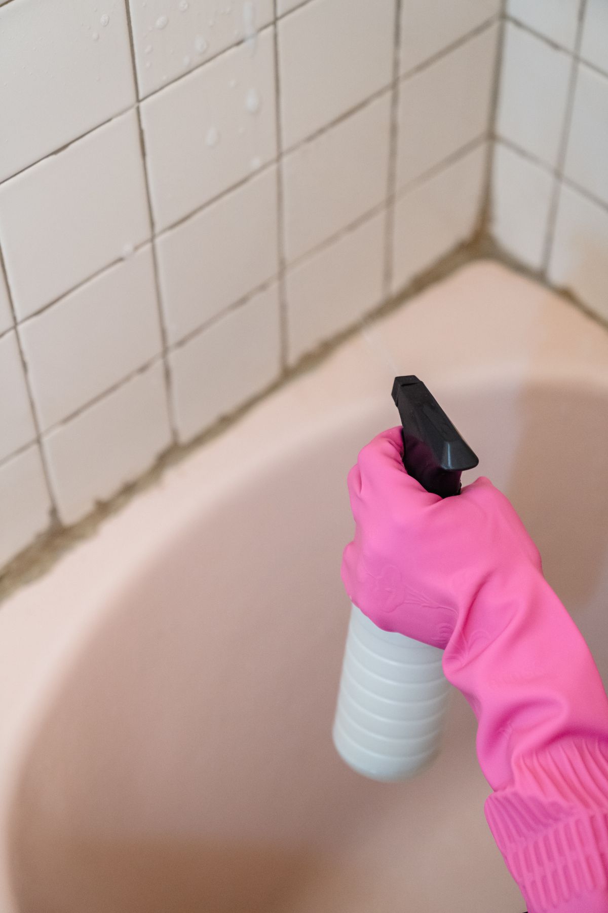 Person in pink gloves cleaning bathroom wall tiles, the white hardness residue that stays when very hard water is conditioned rather than softened