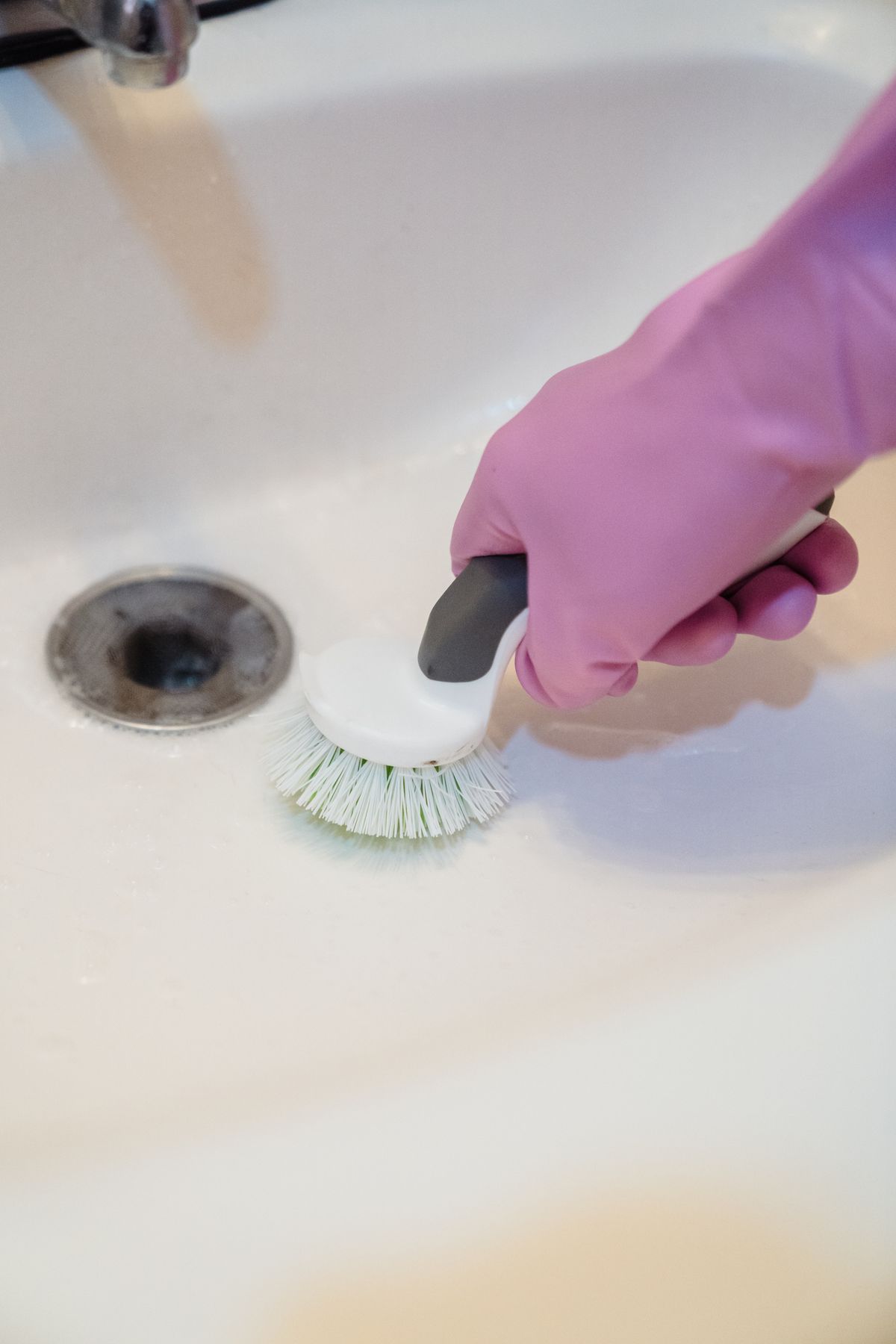 Gloved hand scrubbing a basin with a stiff brush, the hands-on cleaning work a brine tank cleanout requires