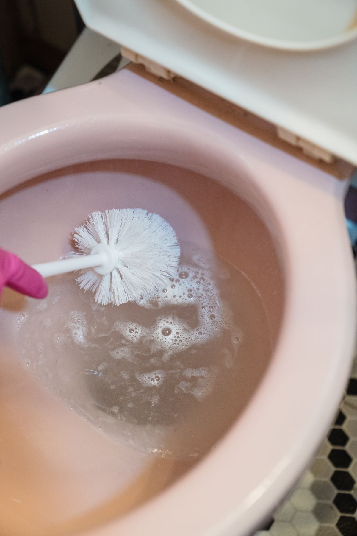 Person scrubbing a foaming toilet bowl with a brush during routine bathroom cleaning