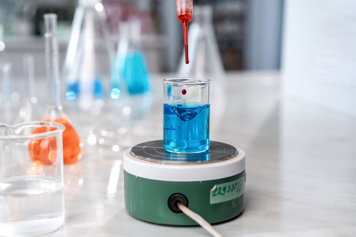 Dropper adding red reagent to a blue solution in lab glassware, the colour-change titration behind a hardness drop test kit