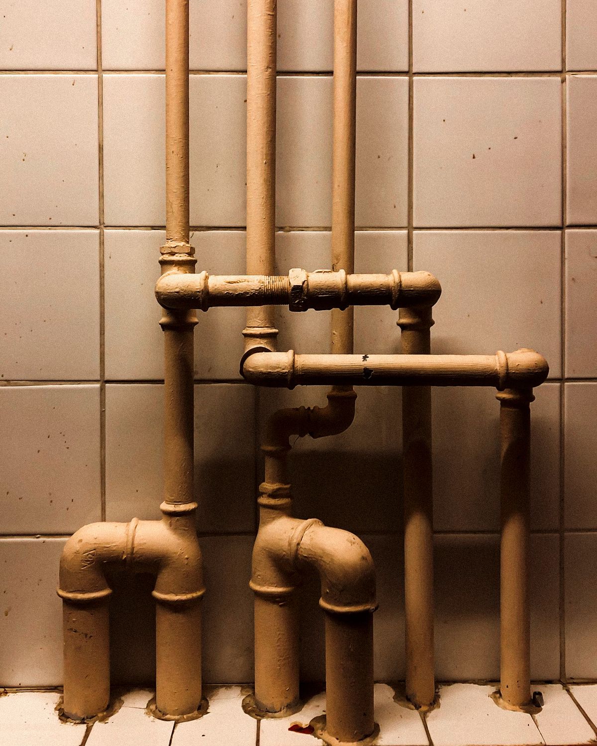 Vertical run of plumbing pipes against a tiled wall, the standing water in long pipe runs that picks up dissolved metal