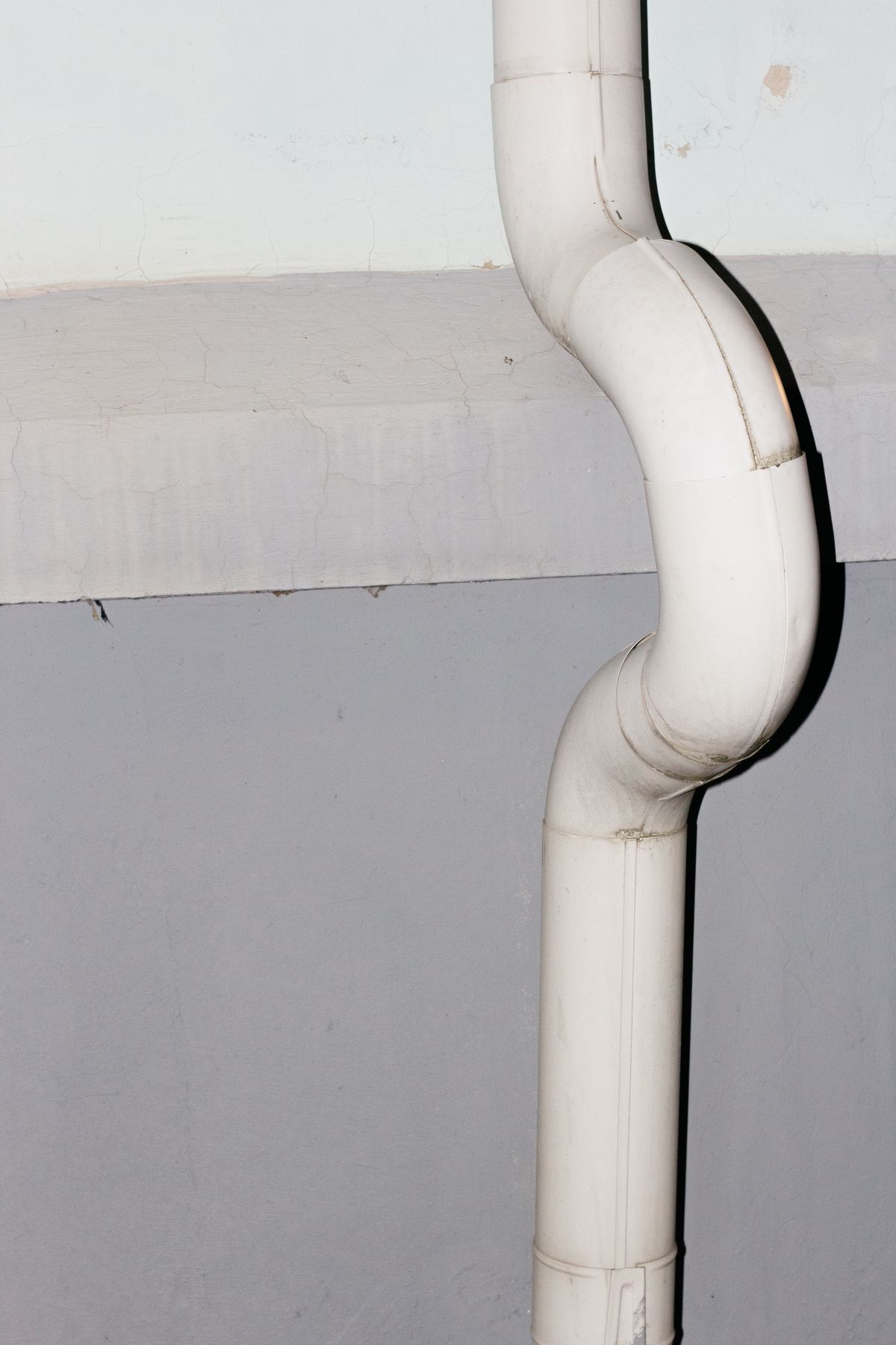 White drainage pipe running down a concrete wall, the drain route that has to carry away everything backwash lifts out of the resin bed