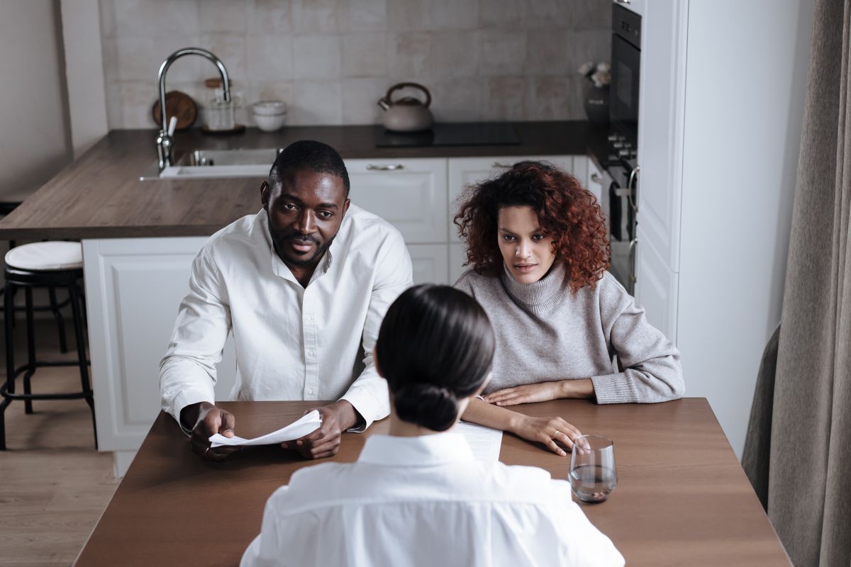 Couple at a kitchen table listening to a representative holding paperwork, the in-home consultation where a RainSoft water softener is usually quoted and financed