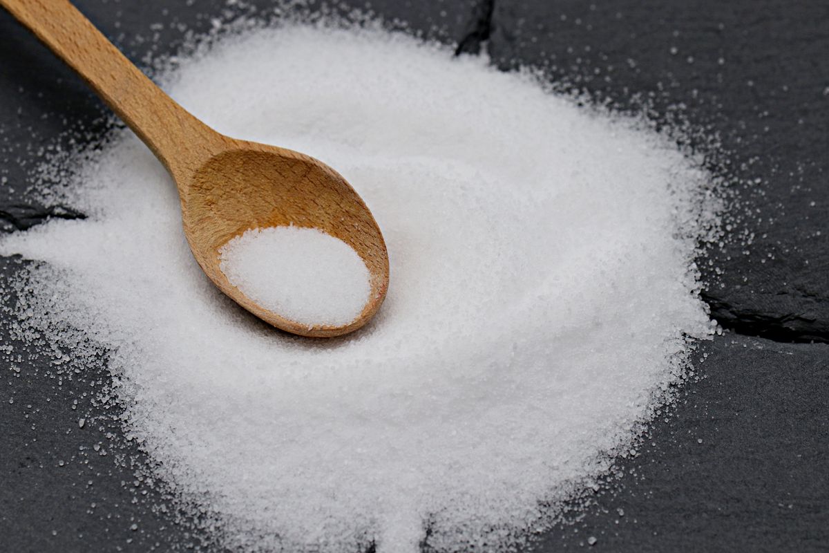 Pile of fine white salt with a wooden spoon on dark slate; sodium chloride brine is what reloads softener resin beads with sodium